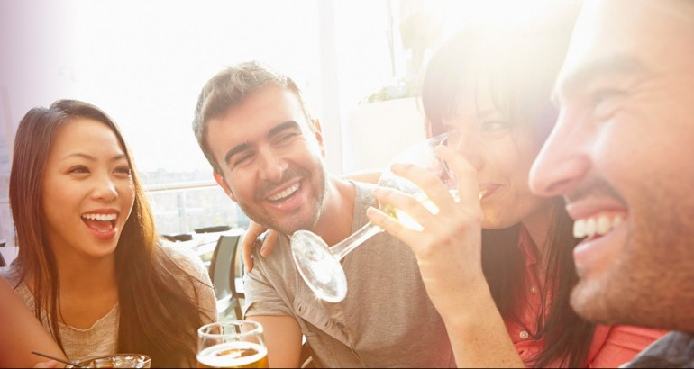 Four friends smiling and socially enjoying alcoholic drinks